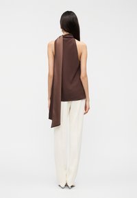 Καφέ αμάνικο τοπ με ντραπέ πλάτη και μακρύ αξεσουάρ, συνδυασμένο με λευκό παντελόνι φαρδιάς γραμμής. Λεία υφή, μινιμαλιστικός σχεδιασμός.