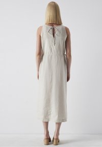 Robe en lin beige à coupe ample, col rond et fente en forme de goutte d'eau au dos. Dispose d'une taille cintrée et d'une longueur mi-mollet.