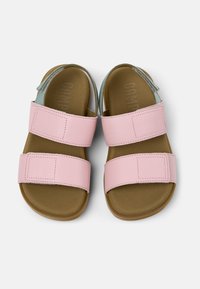 Vaaleanpunaiset nahkasaappaat, joissa on kaksi säädettävää hihnaa, avonainen varvaspäinen muotoilu ja ruskea kumipohja. Sisällä on ruskea teksturoitu jalkapohja.