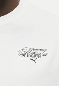 Nærbilde av forsiden på en hvit skjorte med trykt tekst "daily workout: Always Running late" og Puma-logo under teksten.