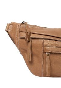 Tan leren heuptasje met een gladde textuur, meerdere ritscompartimenten, decoratieve kwastjes en contrasterende stikseldetails.