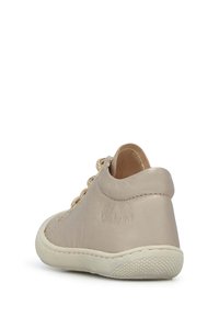 Světle béžová kožená bota s jemnou texturou, nízkým designem okolo kotníku a dekorativními tkaničkami. Obsahuje kontrastní bílou gumovou podrážku a texturovaný grip.