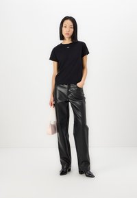 Μαύρη κοντομάνικη μπλούζα με μικρό λογότυπο, συνδυασμένη με γυαλιστερό μαύρο ψεύτικο δέρμα παντελόνι υψηλής μέσης και μια ανοιχτό ροζ τσάντα.