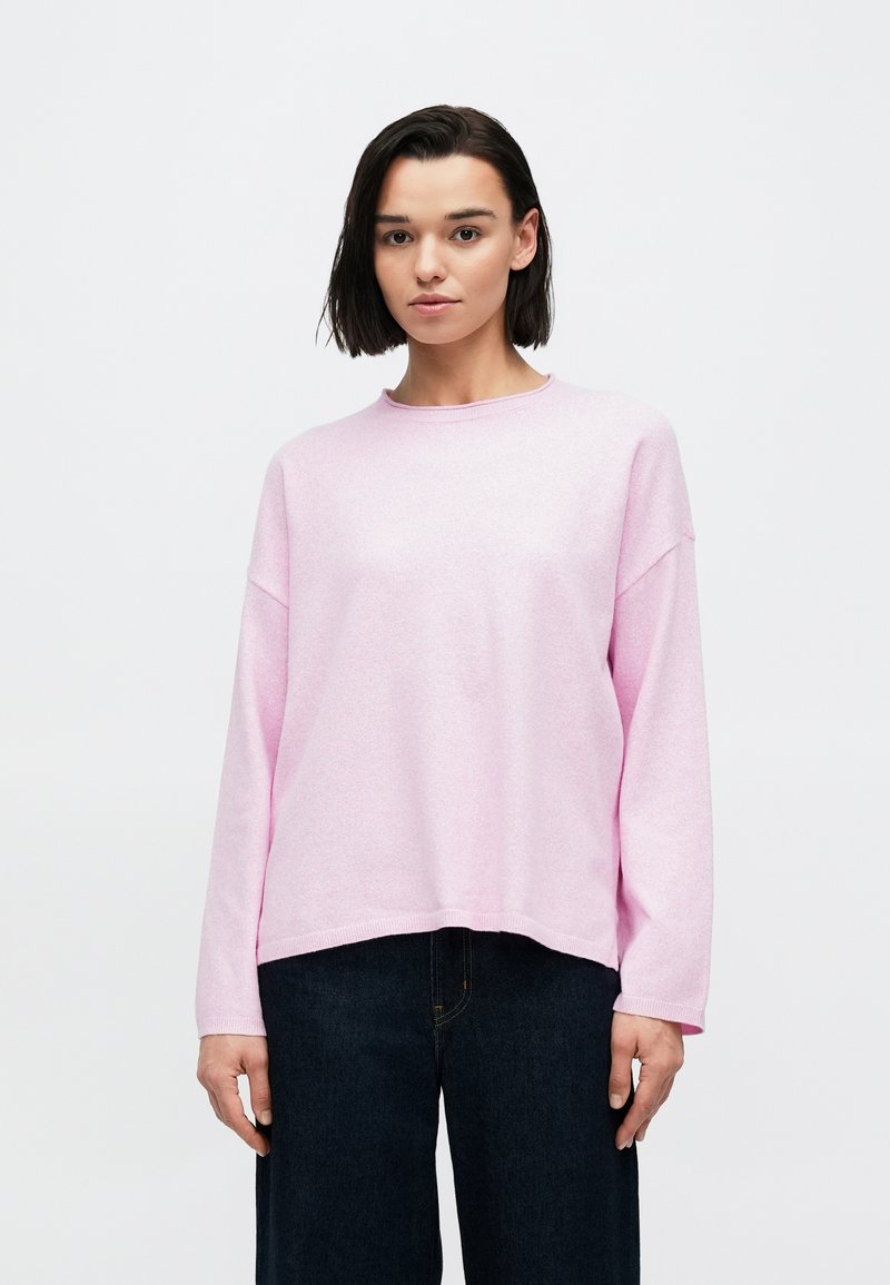 Φαρδιά ροζ πουλόβερ με μακριά μανίκια, στρογγυλή λαιμόκοψη και χαλαρή τελική ραφή, συνδυασμένο με σκούρο τζιν παντελόνι με φαρδιά πόδια. Απαλή, υφή υφάσματος.