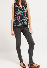 Top sin mangas con estampado floral que presenta un escote en V sobre un fondo oscuro; combinado con vaqueros negros ajustados y sandalias planas.