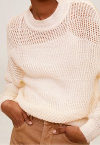 Pull ample de couleur crème en tricot avec un motif texturé à maille ouverte. Comprend un col rond et des poignets côtelés.