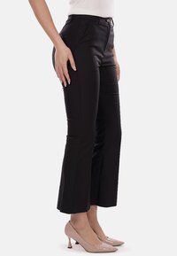 Pantaloni neri su misura con fondo svasato, caratterizzati da una superficie liscia e tasche frontali. Abbinati a tacchi alti nude per un contrasto.