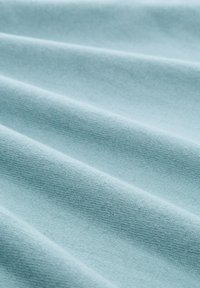 Lichtblauwe stof met een gladde, licht gestructureerde oppervlakte met plooien en kreukels, wat zachtheid en flexibiliteit aangeeft.