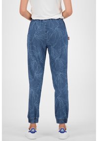 Blaue gemusterte Jogginghosen mit einem Kordelzugbund, elastischen Bündchen und Blattformen auf einem denimähnlichen Stoff, kombiniert mit weißen Sneakers.