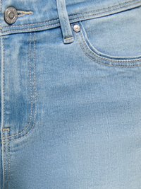 Jean en denim bleu clair en gros plan montrant la poche avant, la boucle de ceinture et le bouton en métal avec les détails des coutures.