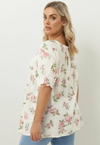 Blommig blus med off-shoulder design, prydd med rosa rosor och gröna blad på en vit bakgrund. Lätt, kort puffärmar.