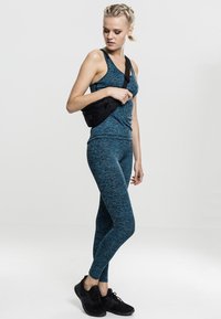 Top sportivo turchese e leggings abbinati con un motivo testurizzato, abbinati a una borsa a tracolla nera e scarpe da ginnastica nere.