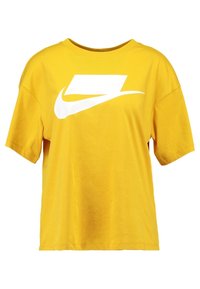 Keltainen lyhythihainen t-paita, joka on valmistettu puuvillasta ja jossa on rento istuvuus. Edessä on suuri valkoinen Nike-logo.