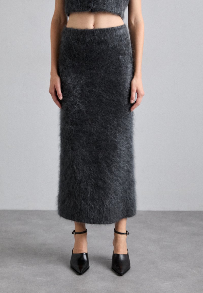 Donkergrijze, fluffy textiel rok met een aansluitende tailleband en rechte silhouet, gecombineerd met puntige zwarte hakken met enkelbandjes.