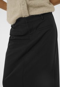 Jupe noire ajustée avec une texture lisse, dotée de poches latérales et d'une coupe structurée. Assortie à un haut en tricot beige clair.