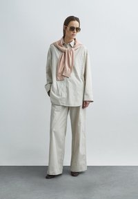 Light-colored striped oversized button-up shirt, beige wide-leg trousers, and a pink sweater tied around the neck, paired with sunglasses.