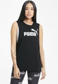 Svart ärmlös linne med stort vitt "PUMA"-logotyp och kattgrafik. Bärs över en grått åtsittande skjorta; matchat med mönstrade leggings.