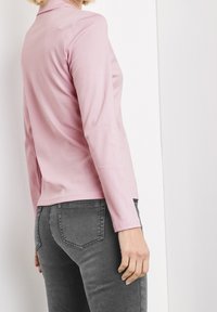 Hellrosa Langarmtop aus weichem Stoff, kombiniert mit dunkelgrauen Jeans. Das Top hat ein schlichtes, eng anliegendes Design mit klaren Linien.