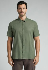 Camisa de manga corta con botones en tela verde oliva con una textura sutil. Presenta un cuello clásico y un dobladillo recto.