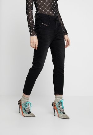 Persoon die een doorschijnende zwarte top met lange mouwen draagt, zwarte slim-fit jeans, glinsterende hoge hakken met turquoise veters en beige sokken met patroon.