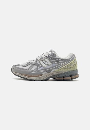 Grauer und weißer New Balance Laufschuh mit Mesh-Obermaterial, gedämpfter Sohle und hellgrünen sowie braunen Akzenten, von der Innenseite gezeigt.