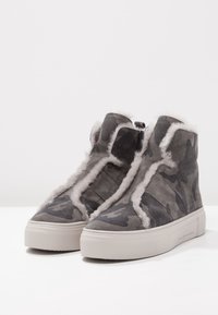 Sneaker alte in camouflage grigio con fodera in pelliccia bianca morbida, esterno in tessuto testurizzato e suola in gomma bianca spessa.