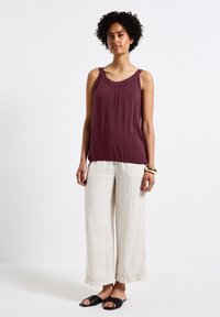 Blusa burdeos sin mangas con detalles fruncidos en el cuello, combinada con pantalones de lino beige de pierna ancha y sandalias negras de tipo slip-on.