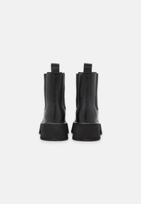 Mustat nahkasaappaat, joissa on jäykkä musta pohja, pystysuorat saumat ja takana lenkilliset vetokahvat helppoa pukemista varten.