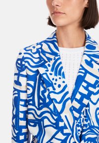 Blazer in Blau und Weiß mit abstrakten Mustern, gefertigt aus strukturiertem Stoff. Verfügt über einen Reverskragen und strukturierte Revers.