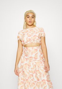 Conjunto de duas peças com um top curto e uma saia em camadas, ambos em um tecido leve com um padrão de paisley em tom pêssego e amarelo.