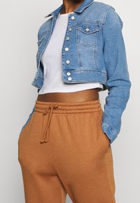 Kort denimjacka i ljusblått med knappstängning fram och två bröstfickor, parat med bruna sweatpants med dragsko.