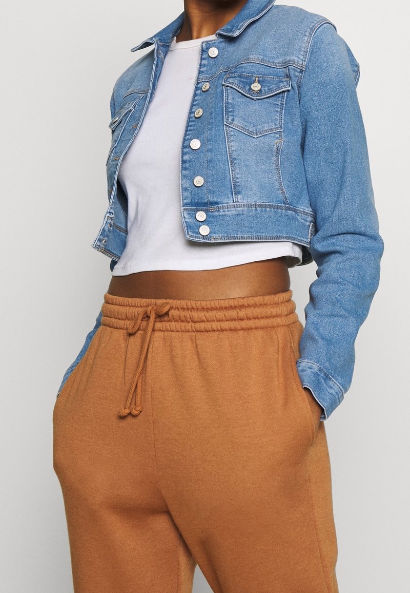 Kort denimjacka i ljusblått med knappstängning fram och två bröstfickor, parat med bruna sweatpants med dragsko.