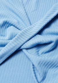 Tissu côtelé bleu clair avec un détail à nouer. Le matériau semble doux et texturé, montrant des lignes et des courbes subtiles dues au pliage.