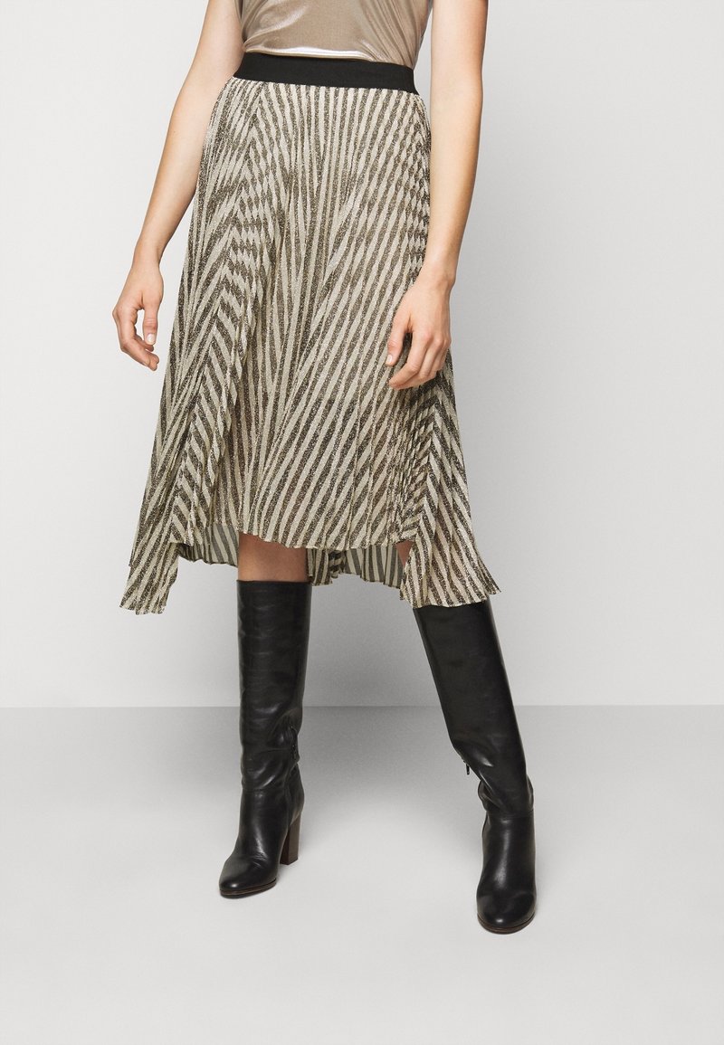 Žena v sukni střední délky béžové a černé pruhované, s černým páskem a černými koženými vysokými botami.