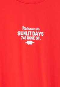 Červené bavlnené tričko s bielym potlačeným textom: "Vitajte na SUNLIT DAYS 745 ROSE ST." s grafickými akcentmi vrátane srdiečok a šípky.