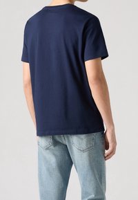Tmavě modré bavlněné tričko s klasickým kulatým výstřihem, krátkými rukávy a rovnými lemy, nošené s světlemodrými džínami.