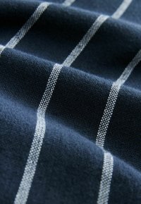 Jūras zila austa auduma ar baltām horizontālām svītrām. Tekstūra šķiet maiga, ar gludu apdari un vienmērīgu rakstu visā virsmā.