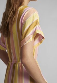 Robe à manches courtes présentant des rayures verticales en rose, jaune et crème. Tissu texturé avec une taille cintrée et un design fluide.
