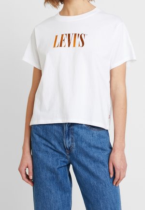 T-shirt bianca in cotone con maniche corte, caratterizzata da un logo arancione di Levi's sul petto. Indossata con jeans di denim blu.