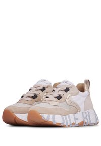 Zapatillas beige y blancas con materiales de ante y malla, con acentos de cordones negros, suela gruesa y texto decorativo en la parte inferior.