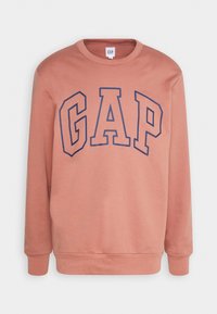 Sudadera de color óxido con cuello redondo, mangas largas y un destacado logo en azul marino de "GAP" en la parte frontal. Textura suave.