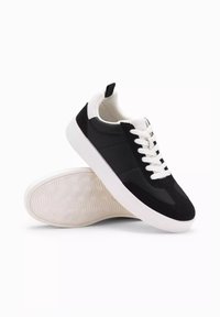 Svartvita sneakers med en slät yta, strukturerade svarta accenter, vita snören och en gummisula med ett fiskbensmönster.