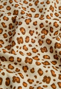Leopárdmintás anyag bézs háttérrel, amelyen szabálytalan barna foltok láthatók eltérő árnyalatokban, puha, texturált szövettel.