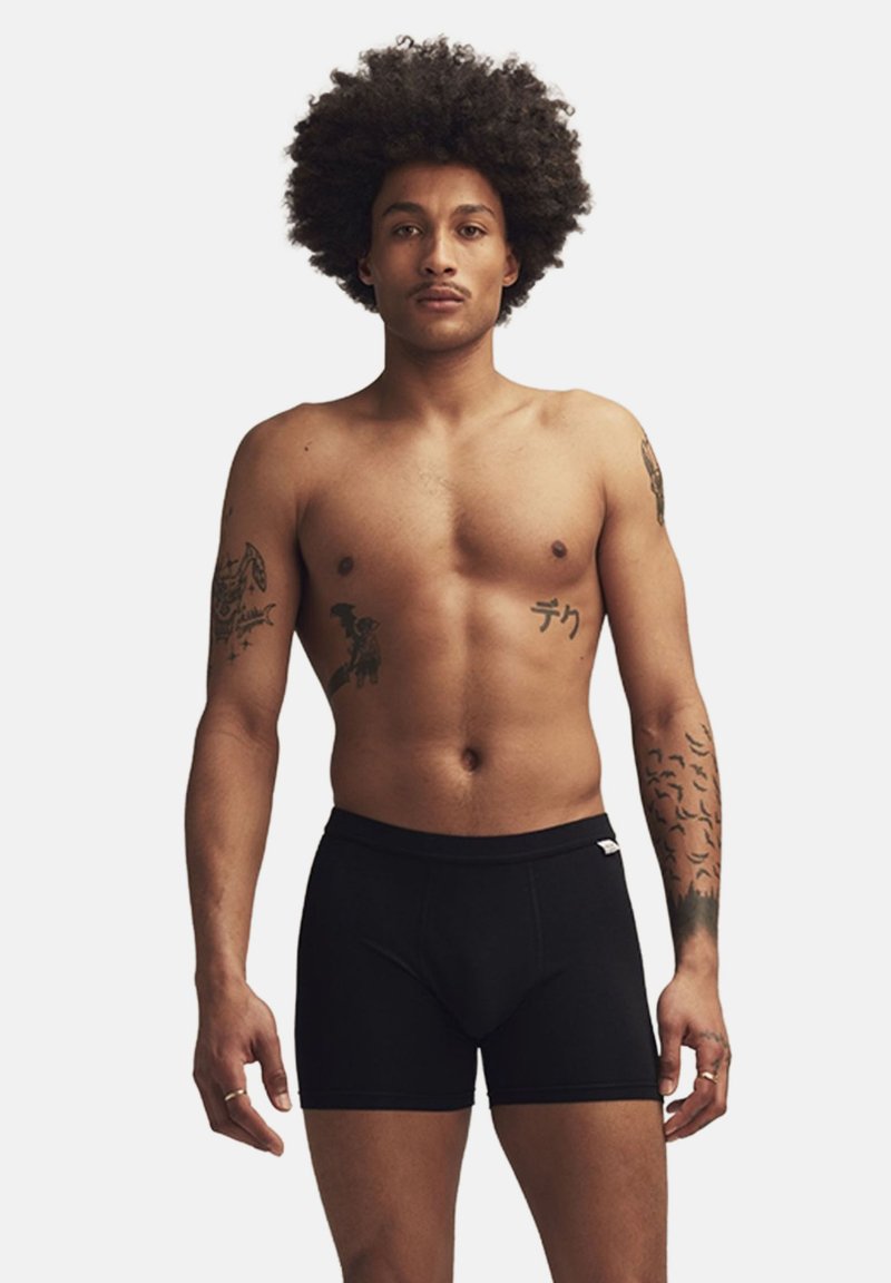Svarta boxershorts i mjukt tyg, med en snug passform och elastisk midja, visade på en manlig modell med en naturlig fysik.