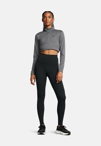 Γκρι μπλουζάκι με φερμουάρ στο τέταρτο και μακριά μανίκια, συνδυασμένο με μαύρο κολάν ψηλόμεσο. Και τα δύο κατασκευασμένα από ελαστικό ύφασμα που απομακρύνει την υγρασία. Μαύρα αθλητικά παπούτσια.