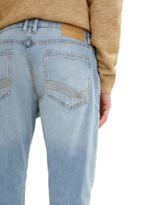Jeans din denim de un albastru deschis, cu o croială îngustă, având două buzunare la spate cu cusături decorative și o etichetă din piele bej la talie.