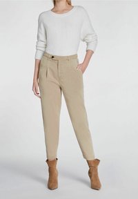Pantalons beiges taille haute avec poches latérales, jambes fuselées et plis à l'avant, associés à un pull blanc texturé et des bottines beiges.