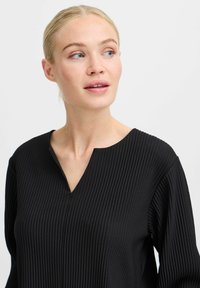 Black ribbed top with a V-neckline, featuring long sleeves and a textured fabric. Smooth finish and structured shape.