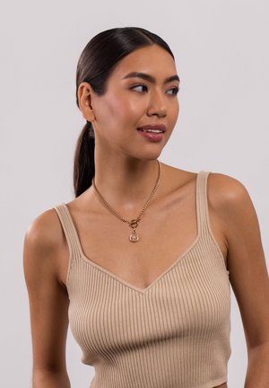 Beige geribbelde crop top met een diepe V-halsontwerp. G gedragen met een gouden ketting met een cirkelvormige hanger. Gladde textuur.