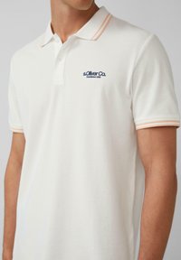 Weißes Polo-Shirt aus Baumwolle mit orange gestreiftem Kragen. Verfügt über ein gesticktes s.Oliver Co. Logo auf der Brust. Klassische Passform und kurze Ärmel.